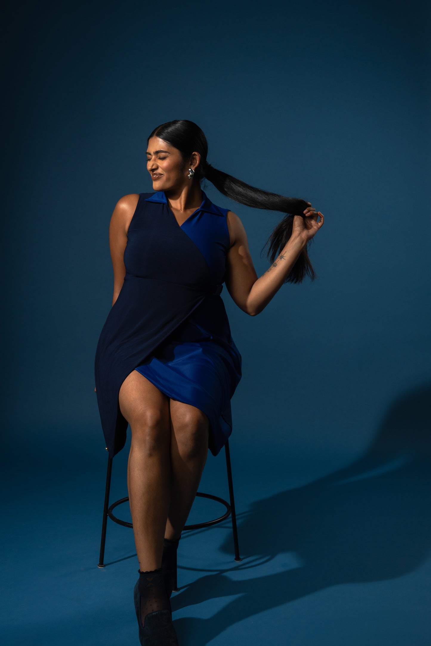 Woman in a blue dress standing on a stool against a dark blue background
