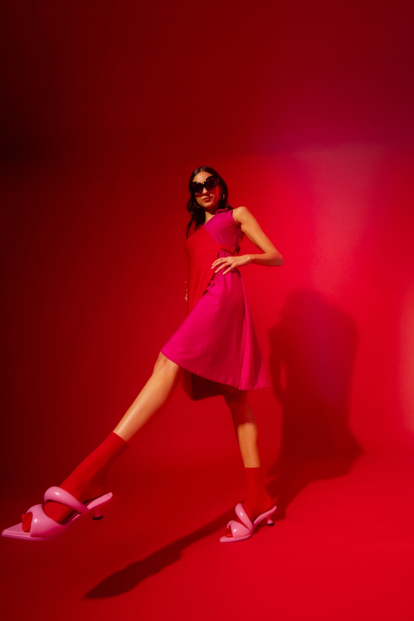 Woman in a pink dress and shoes standing against a red background