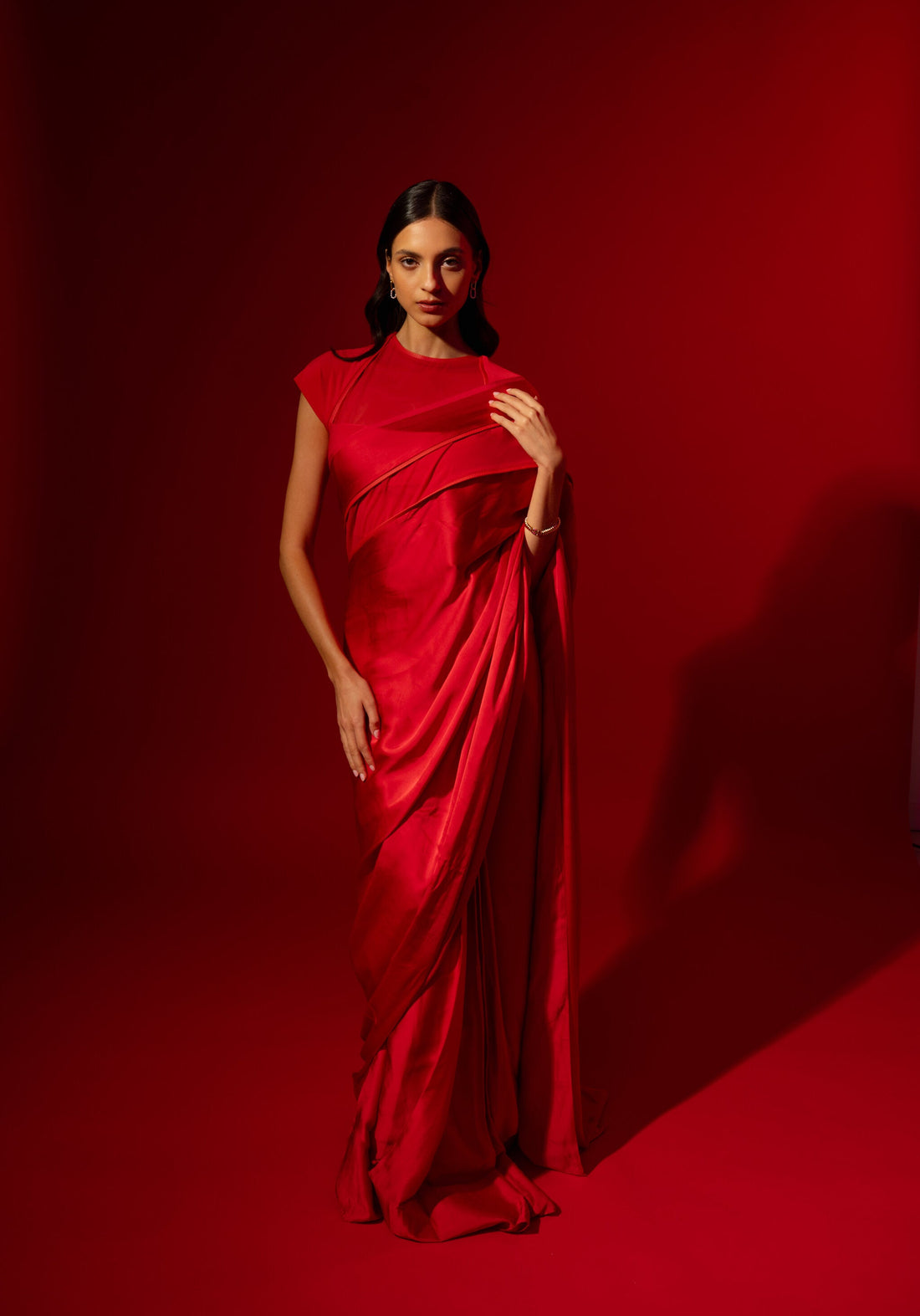 Woman wearing the Rebel Roots Capsule Sari in red, a pre-draped satin saree, standing against a red background