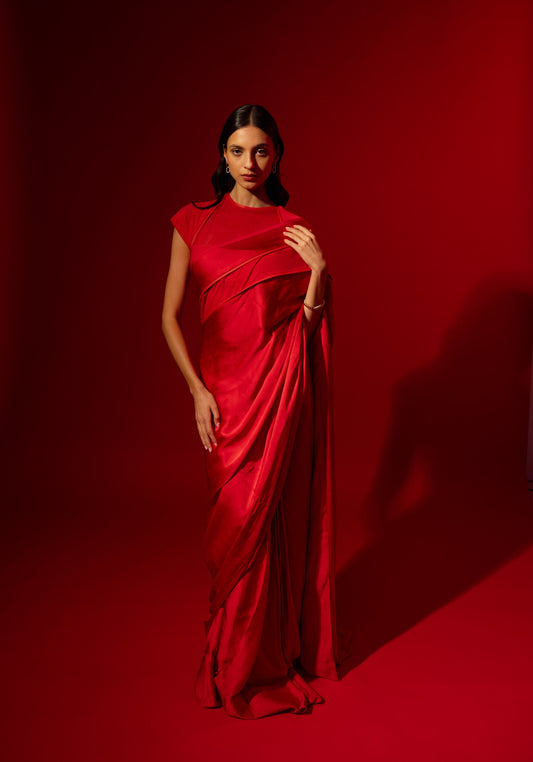 Woman wearing the Rebel Roots Capsule Sari in red, a pre-draped satin saree, standing against a red background