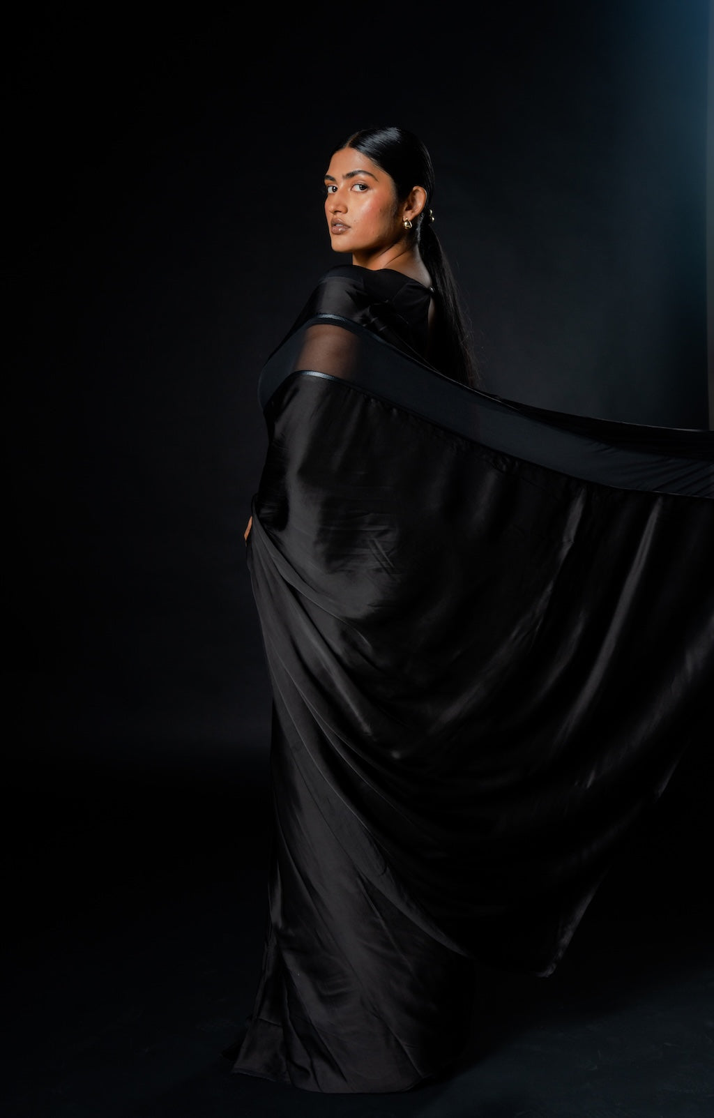 Woman posing in an easy ready to wear black saree against a dark background. The saree is a part of the Label Rebel Roots Capsule Collection for the modern Indian woman
