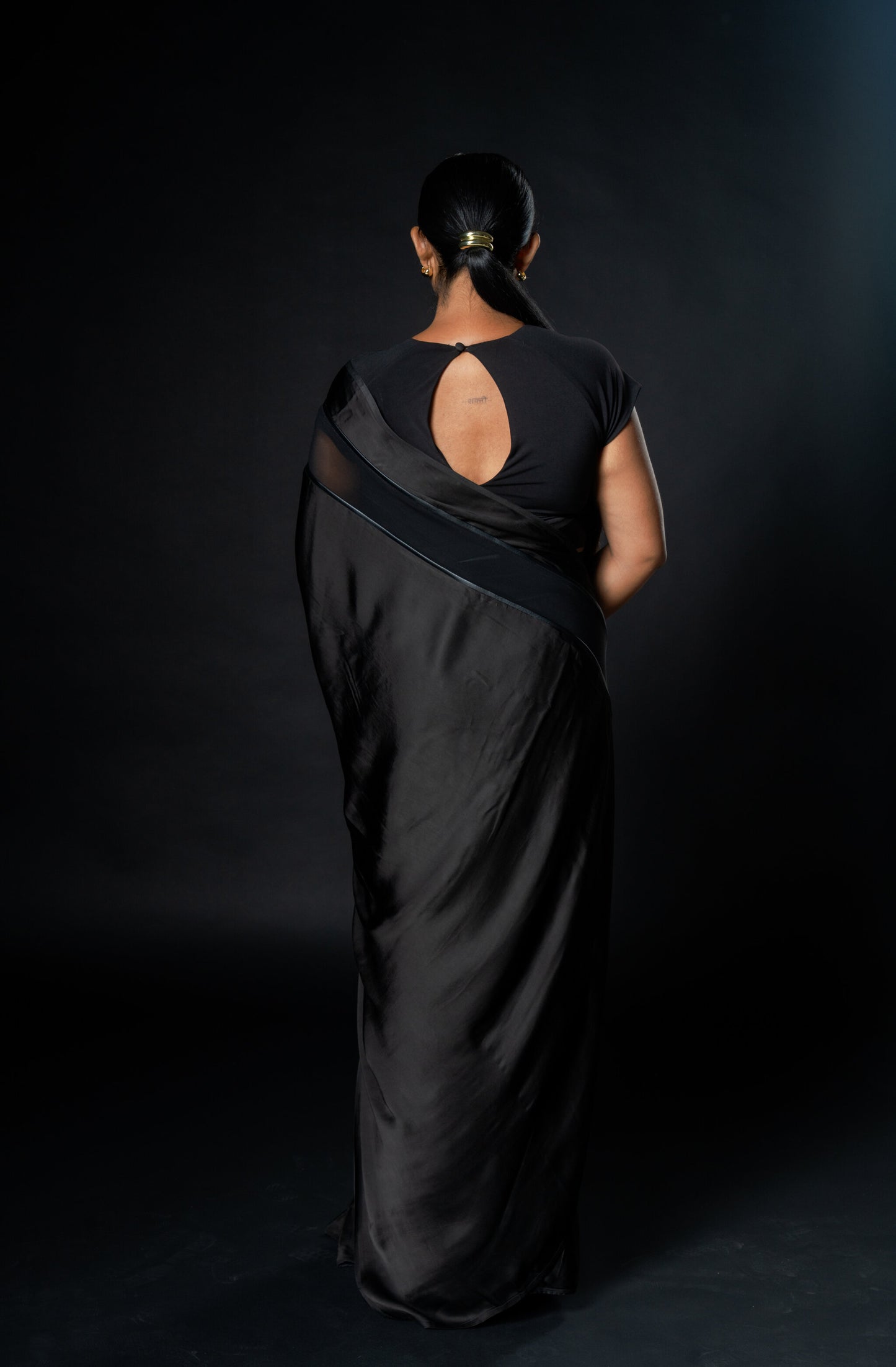 Woman wearing a black saree with a plain background