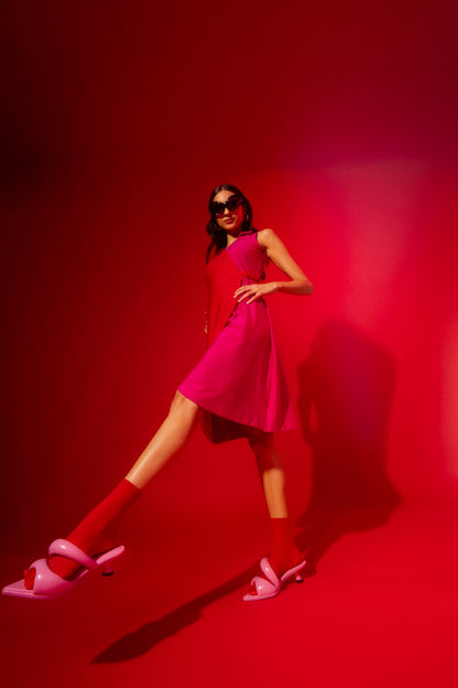 Woman in a pink dress and shoes standing against a red background