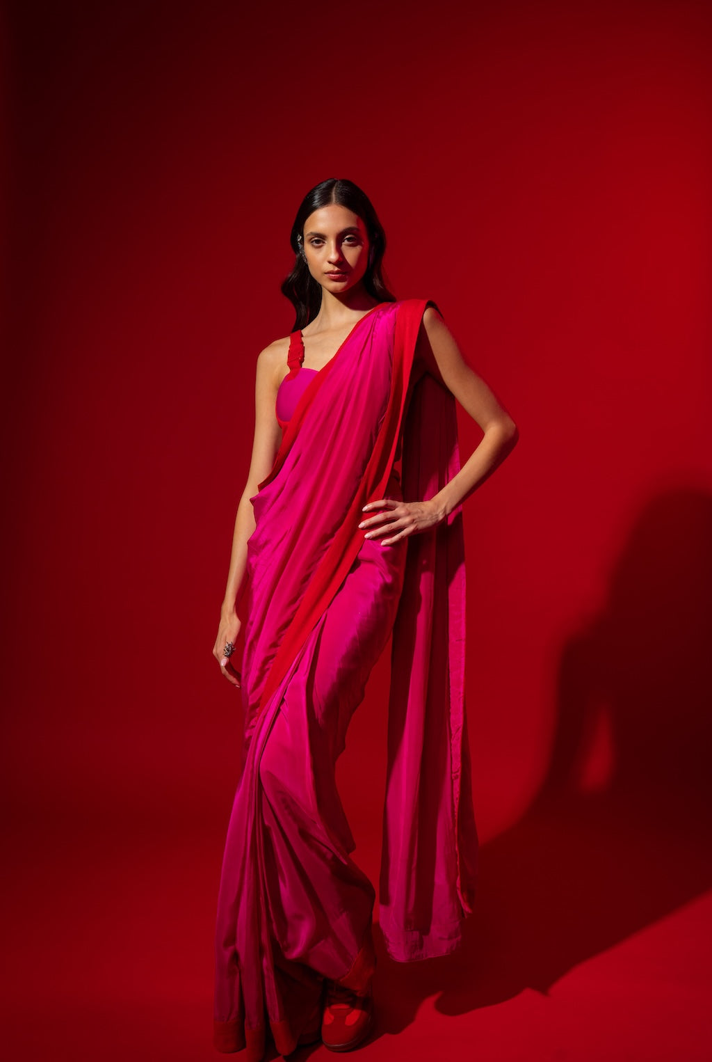 Woman wearing a bright pink saree  (Rebel Roots Ready to wear Buckle Saree) against a red background