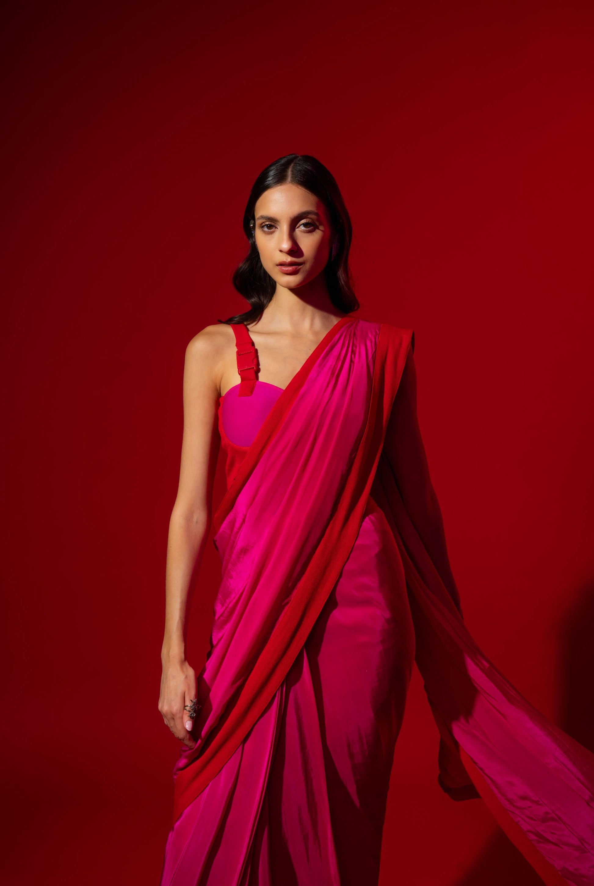 Woman wearing a bright pink saree against a red background