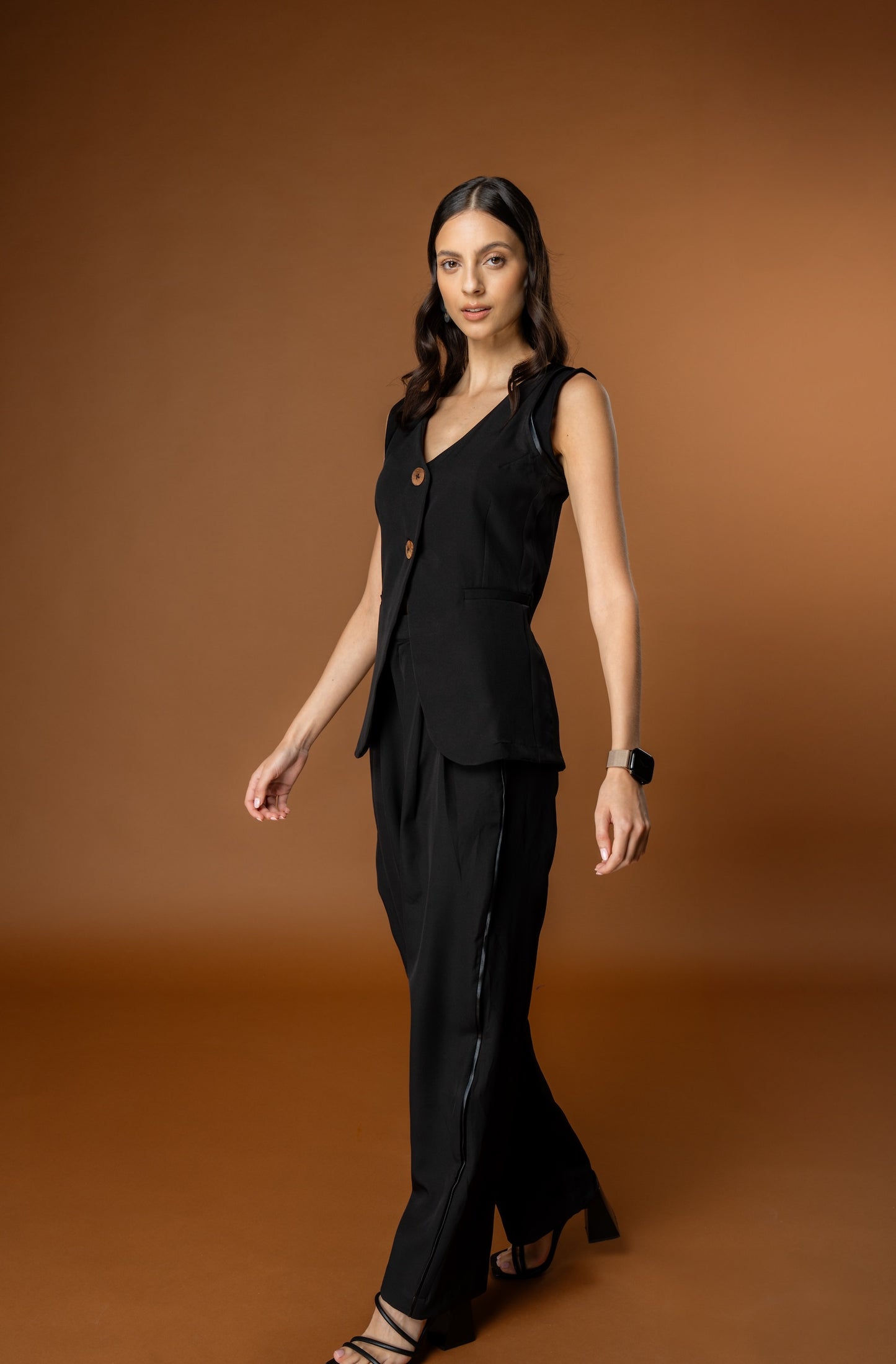 Woman wearing Rebel Roots PowerSet black outfit (Black Waistcoat and Black Pants) against a brown background.