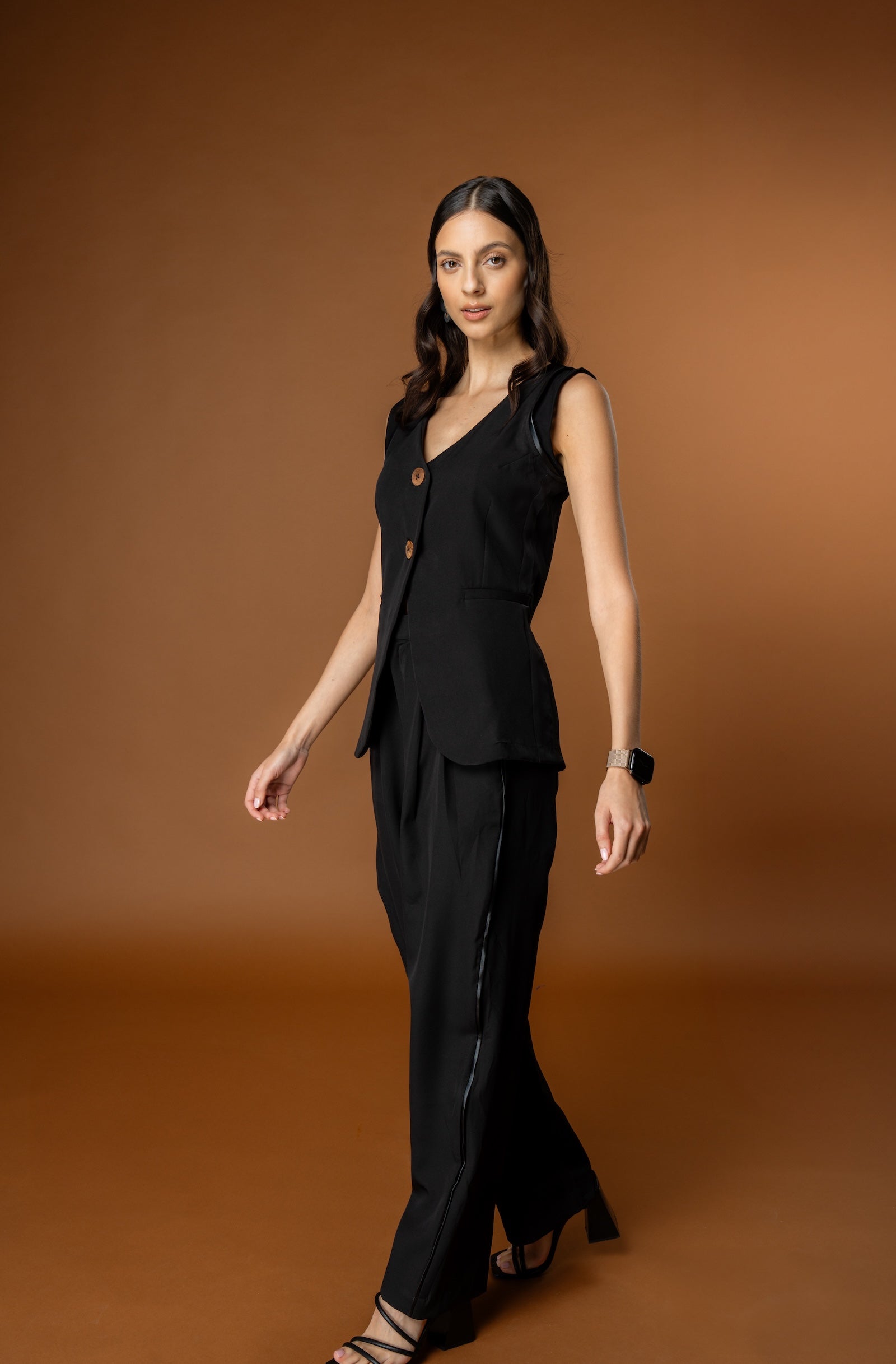 Woman wearing Rebel Roots PowerSet black outfit (Black Waistcoat and Black Pants) against a brown background.