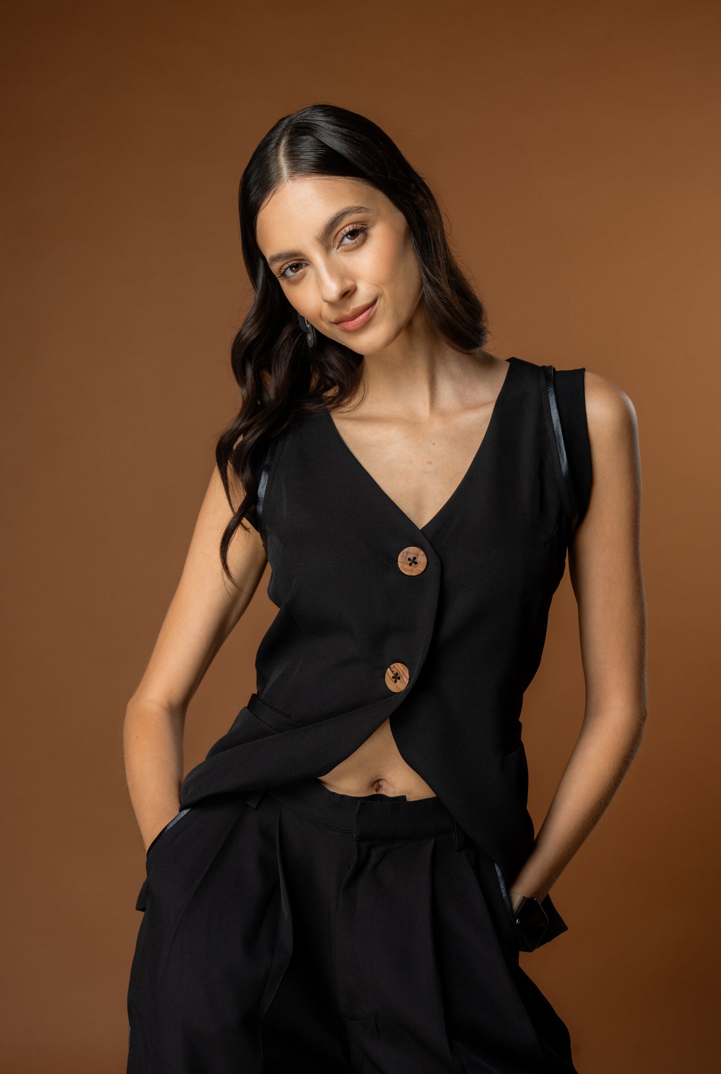 Woman wearing a black sleeveless waistcoat and black trousers with deep pockets. The coord set is a part of the Rebel Roots Capsule Powerset collection