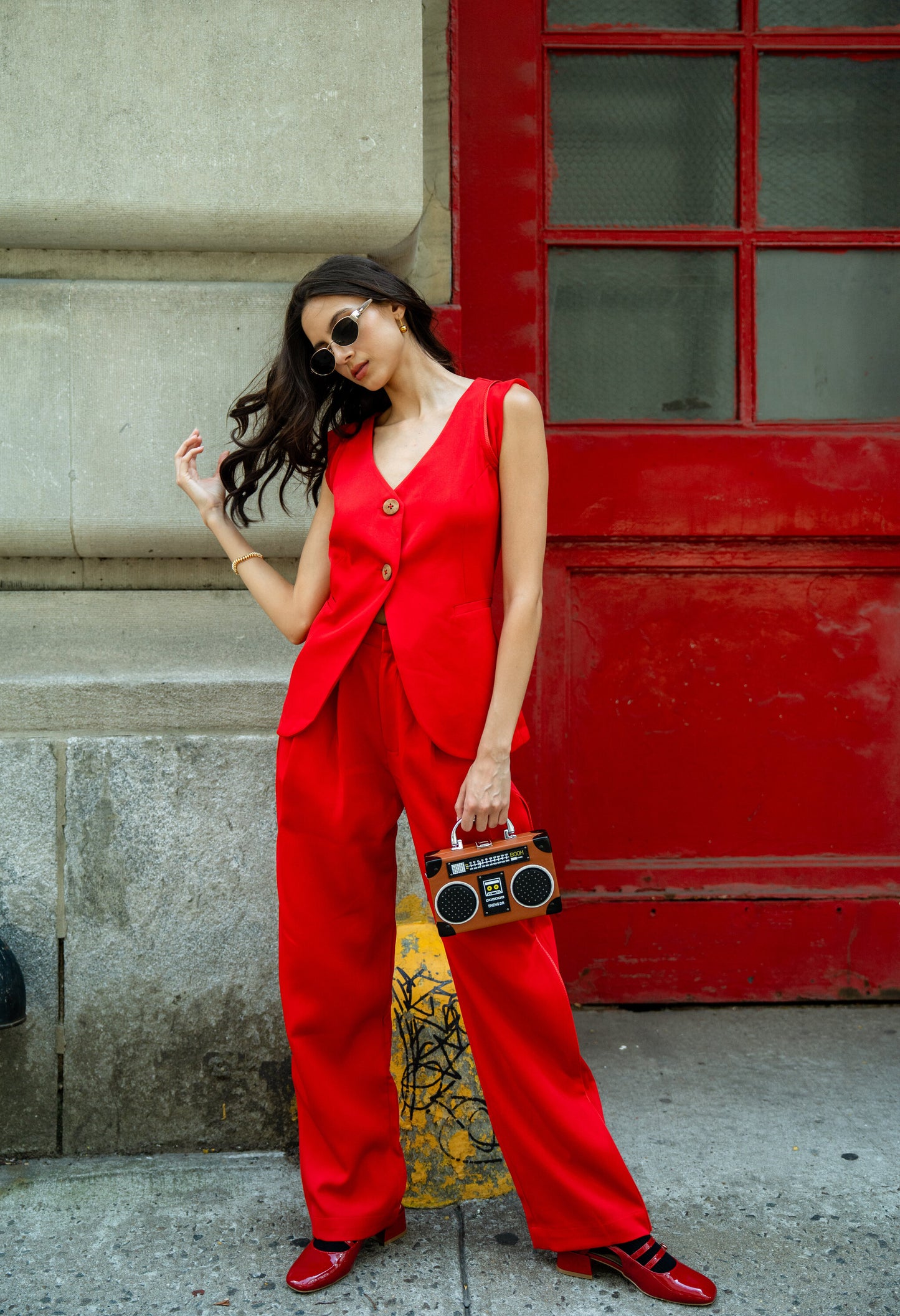 Woman in a red Rebel Roots Capsule Powerset outfit holding a boombox style bag, against a red door.