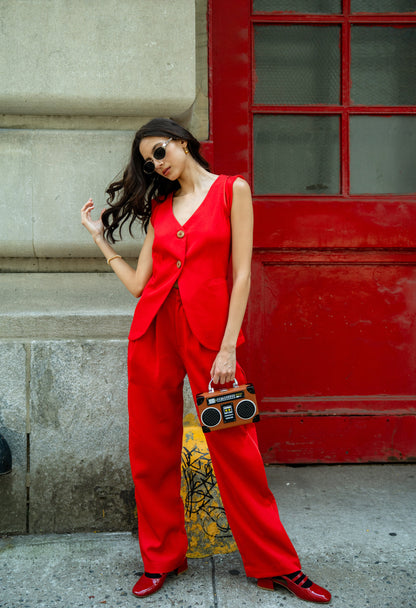 Woman in a red Rebel Roots Capsule Powerset outfit holding a boombox style bag, against a red door.
