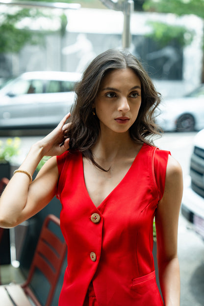 Woman wearing a red sleeveless waiscoat with brown buttons, standing outdoors.