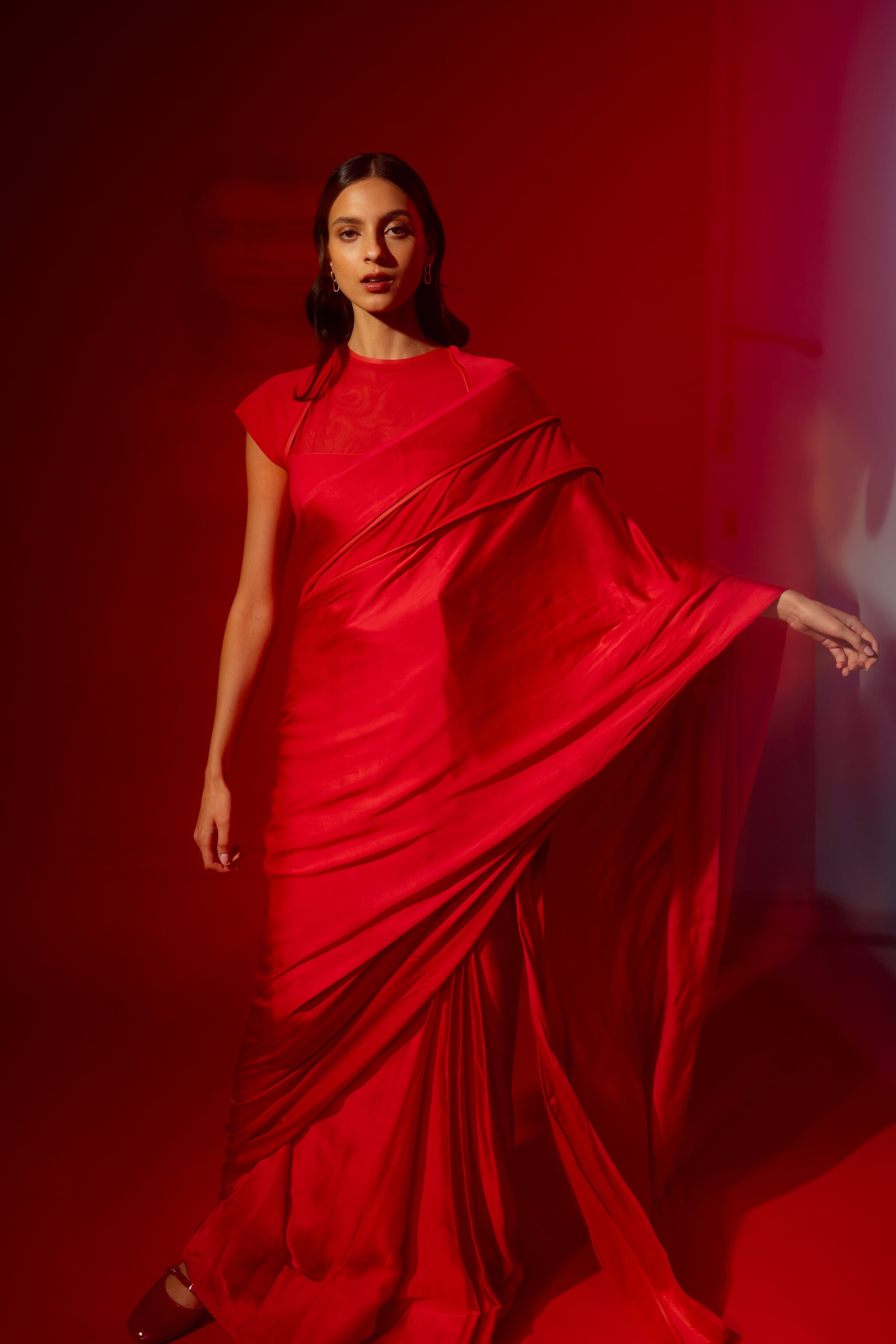 Woman wearing a ready to wear red saree posing against a red background. 