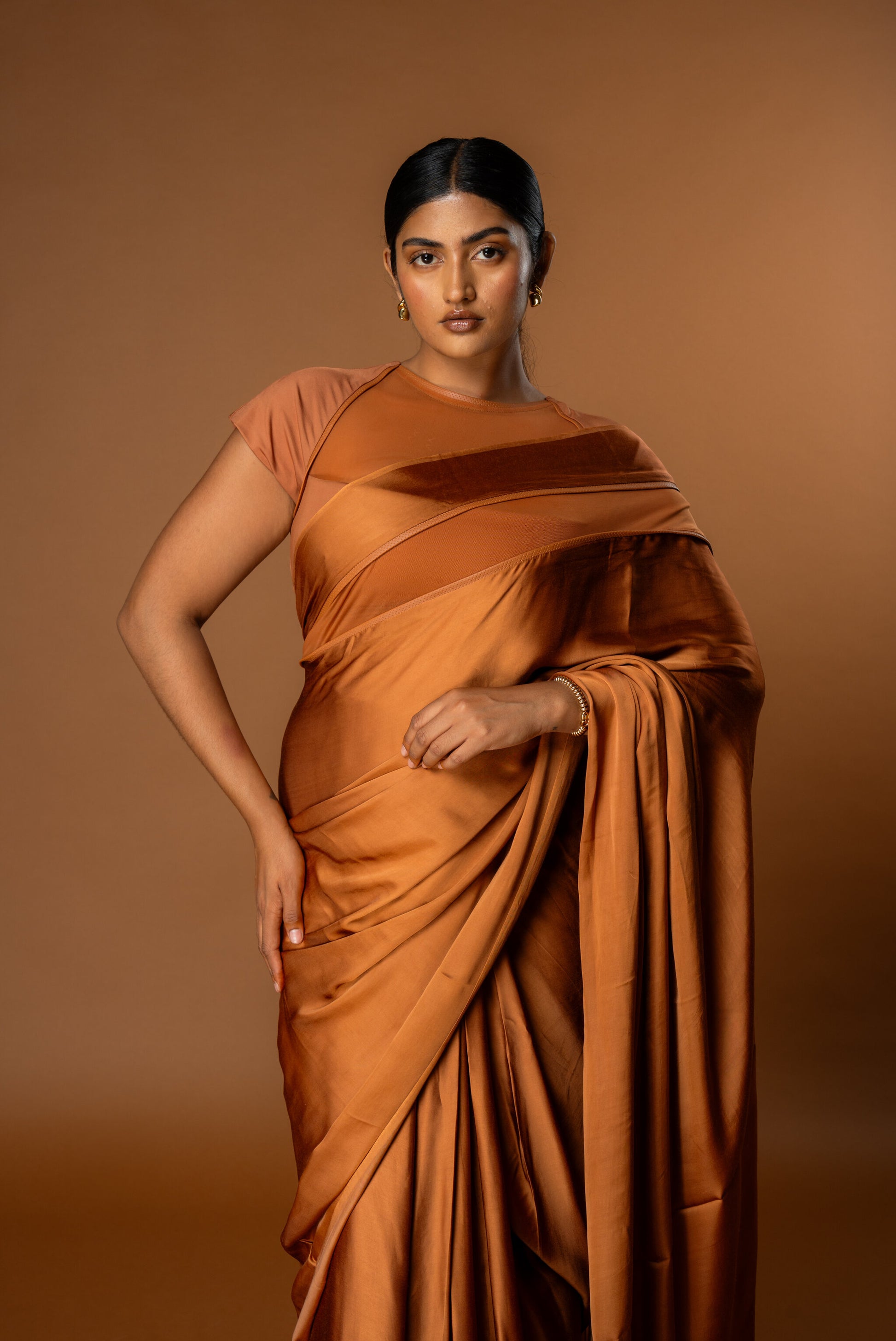 Woman wearing Rebel Roots Tan saree against a brown background. The blouse and Saree are pre-stitched and Ready to Wear. 